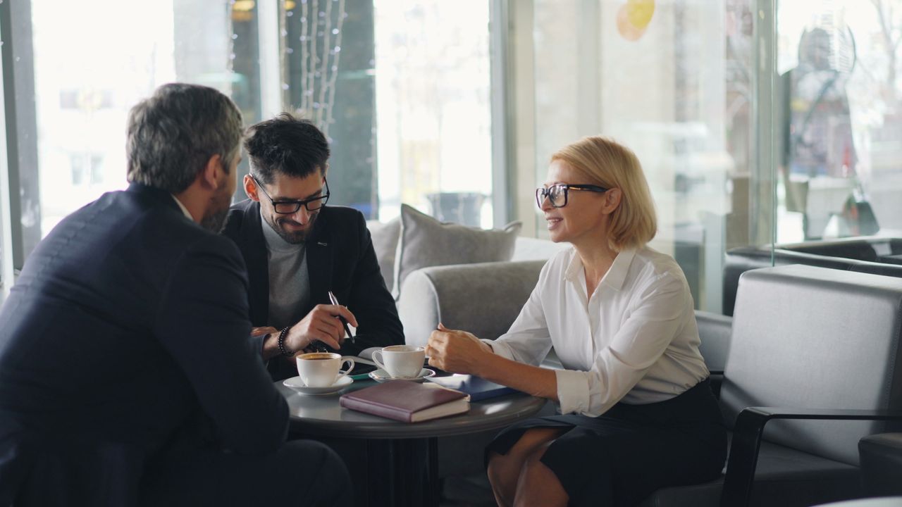 Three professionals engaged in a business meeting at a cafe.